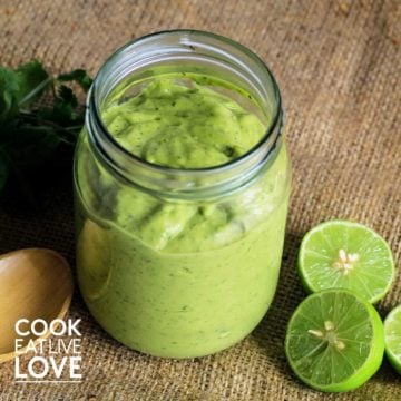 Jar on creamy avocado sauce with limes and parsley on burlap.