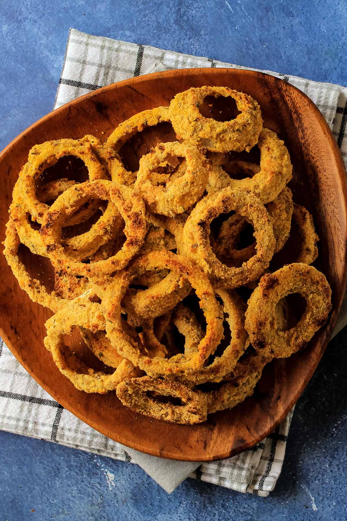 Platter of onion rings on plate with a hand reaching to grab one.