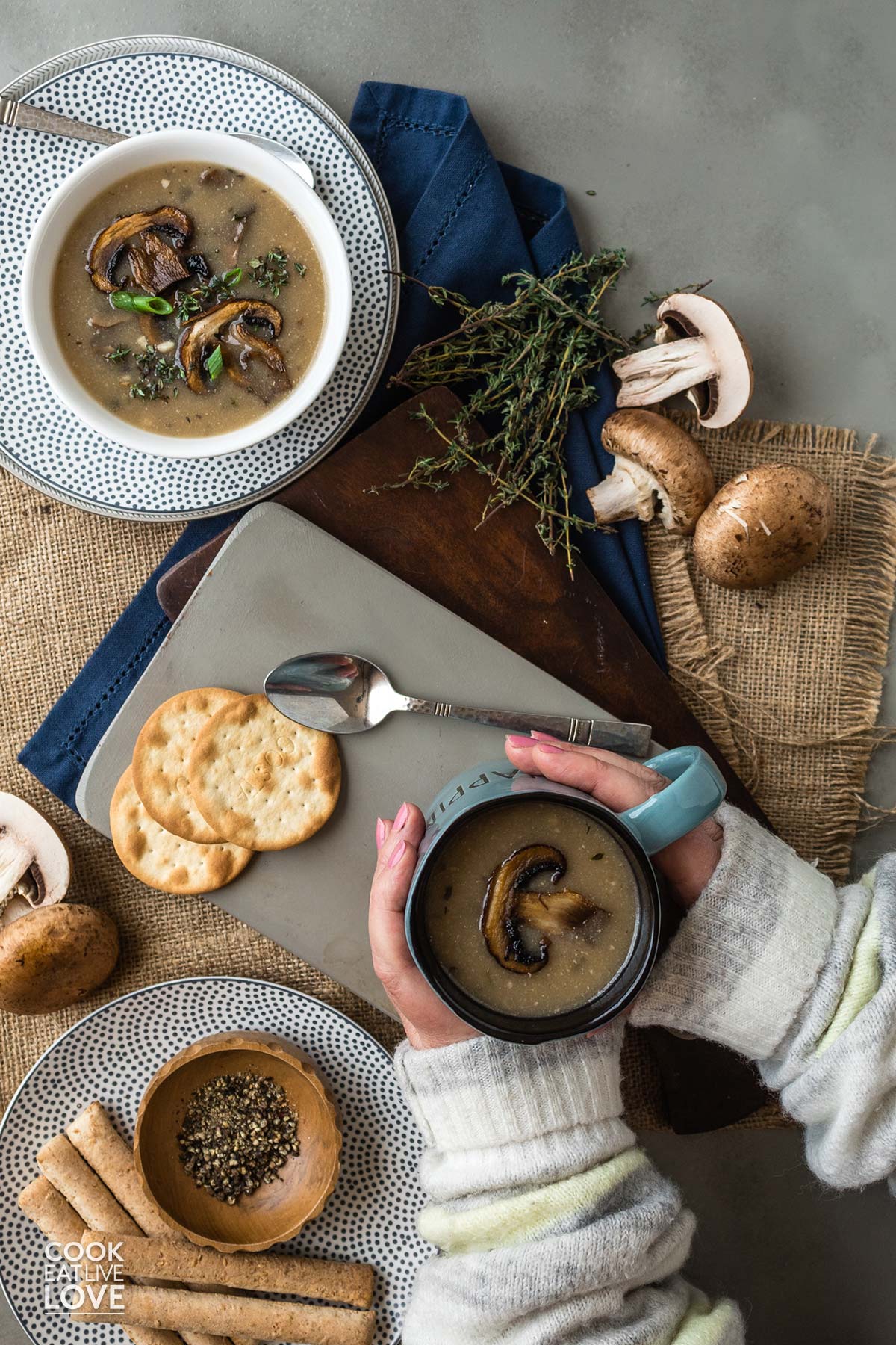 Creamy mushroom soup in wooden bowl with wooden spoon, surrounded by green onions and whole mushrooms.