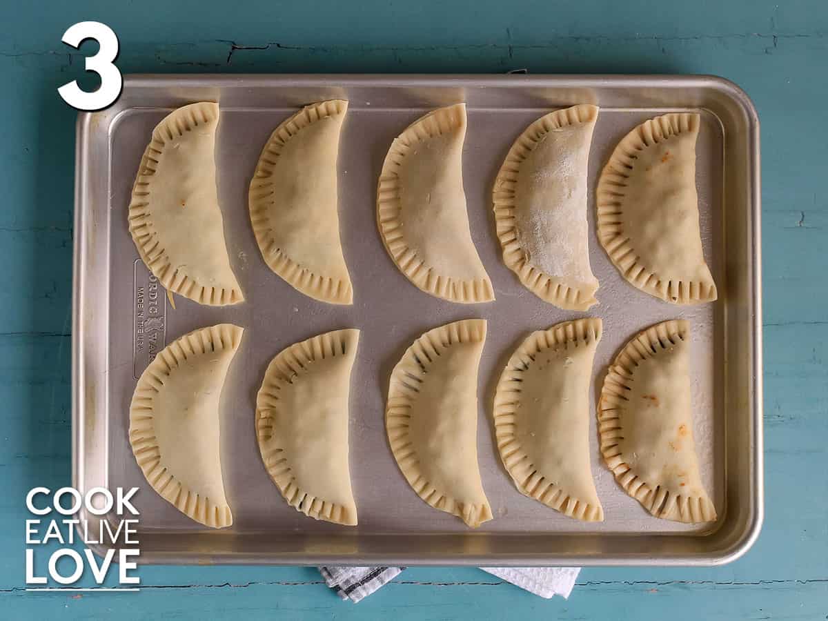 Folded empanadas are lined up on a baking tray.