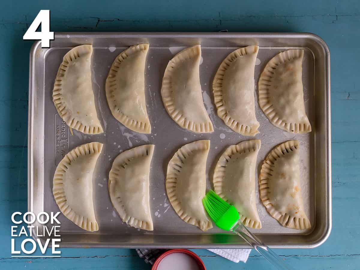 Vegetarian empanadas on tray with milk to the side and a pastry brush laying on edge of tray.