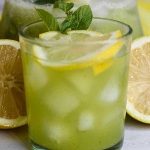 Glass of cucumber lemonade in front of lemons cut in half.
