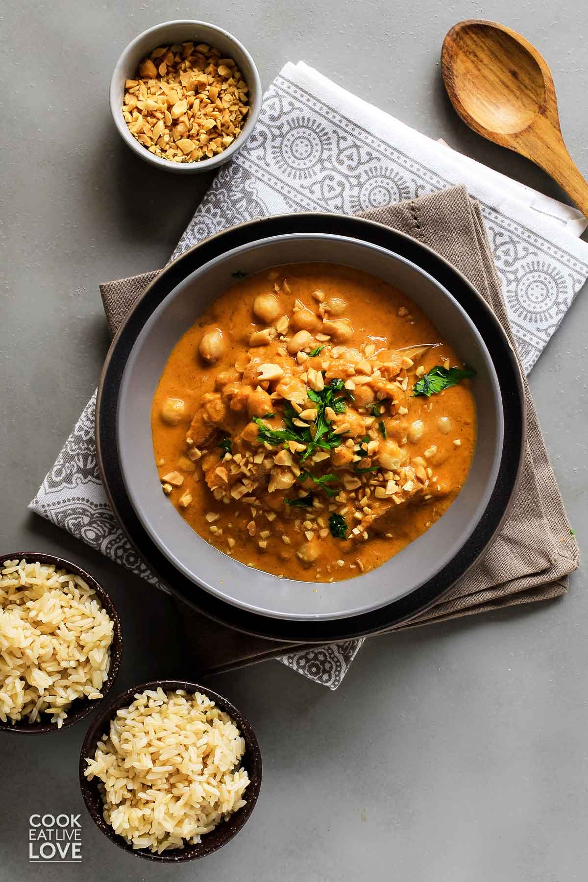 Vegan massaman curry in bowl with chopped peanuts and small bowls of brown rice.