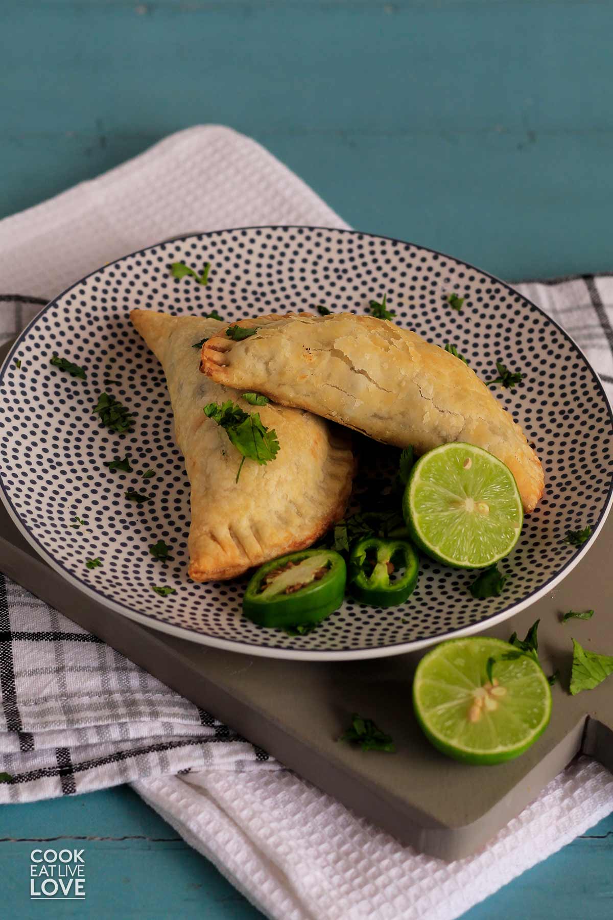 Overhead of cooked and ready empanadas on rectangle and white gray polka dot plates.