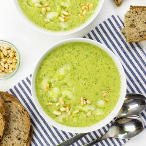 Bowl of green soup on a blue and white napkin with spoon.