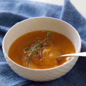 Bowl of butternut squash soup with spoon and fresh rosemary.