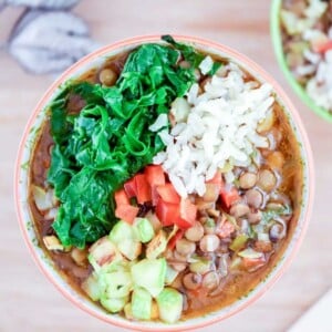 Bowl of lentil stew topped with tomatoes, avocado and spinach.