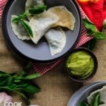 Overhead view of wonton raviolis ready to eat on plates, garnished with basil and served up with sauce.