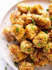 Overhead view of white plate of breaded cauliflower in sauce piled up. Garnished with green flakes.