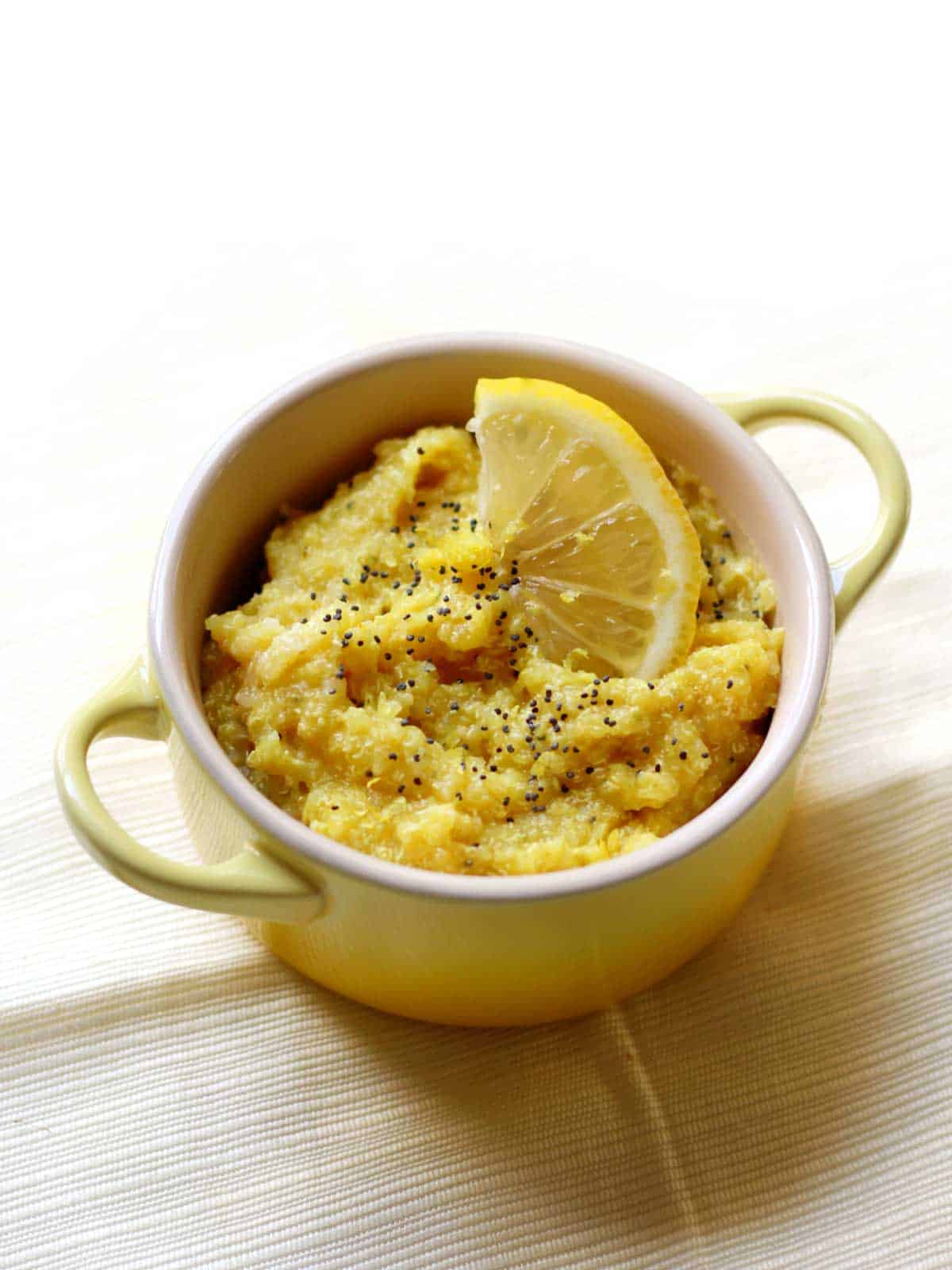 Yellow mug with two handles filled with quinoa flakes garnished with lemon slices.