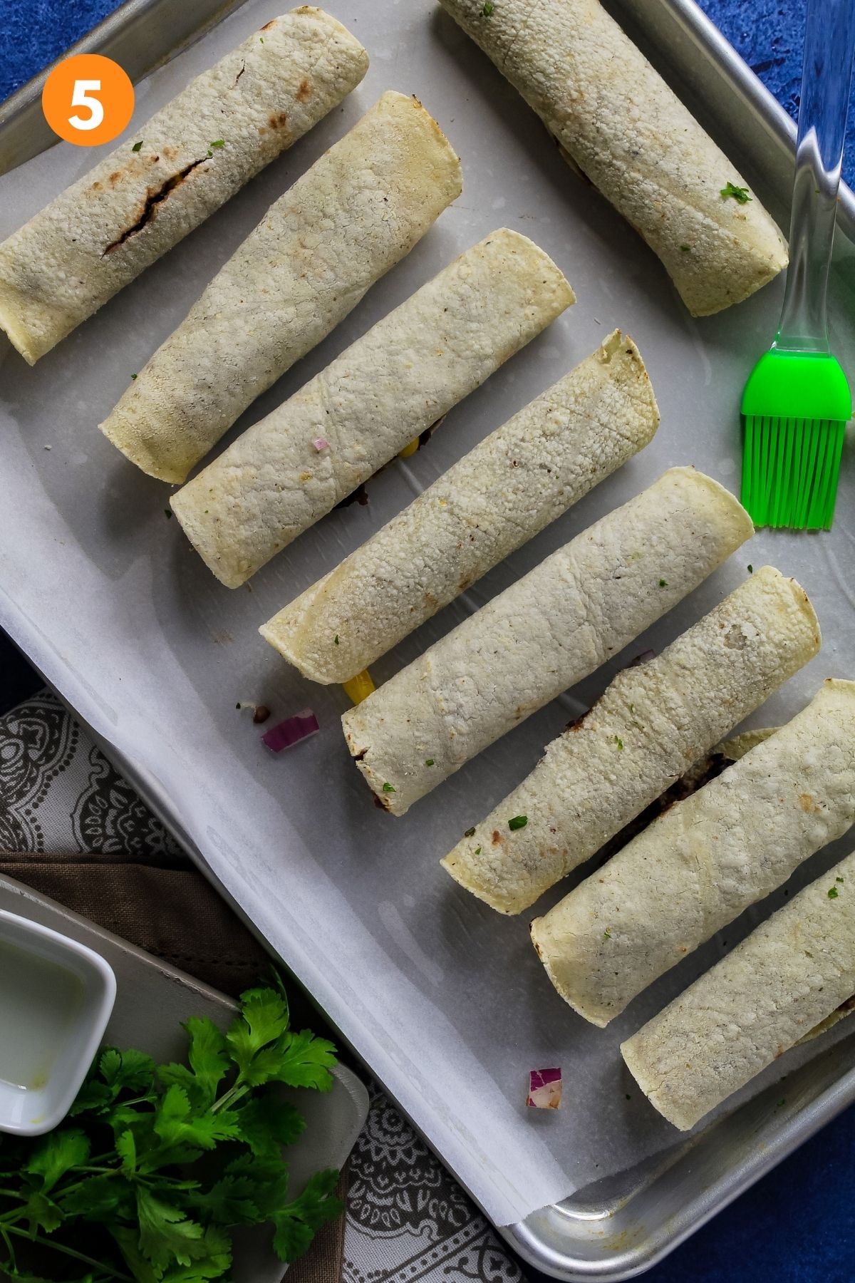 Rolled uncooked taquitos on baking sheet.