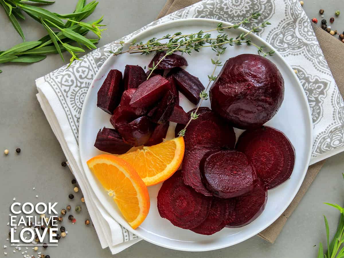 Beets, whole, sliced and quartered on a plate with orange and herbs