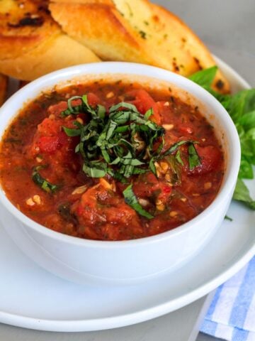 A bowl of hearty marinara sauce on a plate with toasted bread.