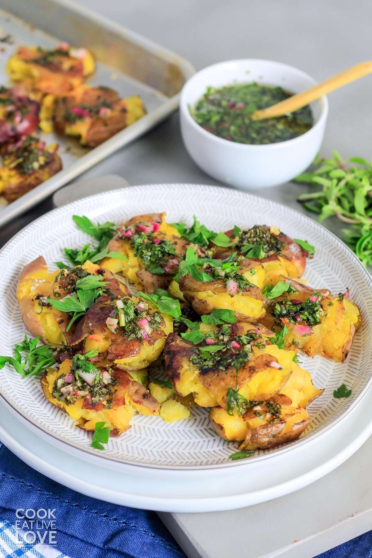 A plate of smashed red skin potatoes on a plate with chimichurri drizzled on top and fresh parsley. 