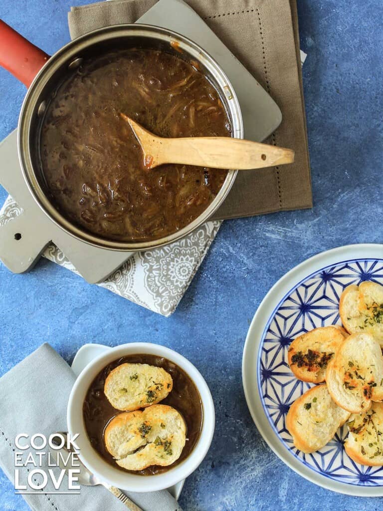 Vegan french onion soup served up in pot and a bowl topped with croutons