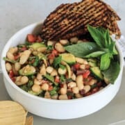 White bowl with cannellini salad garnished with basil and grilled bread