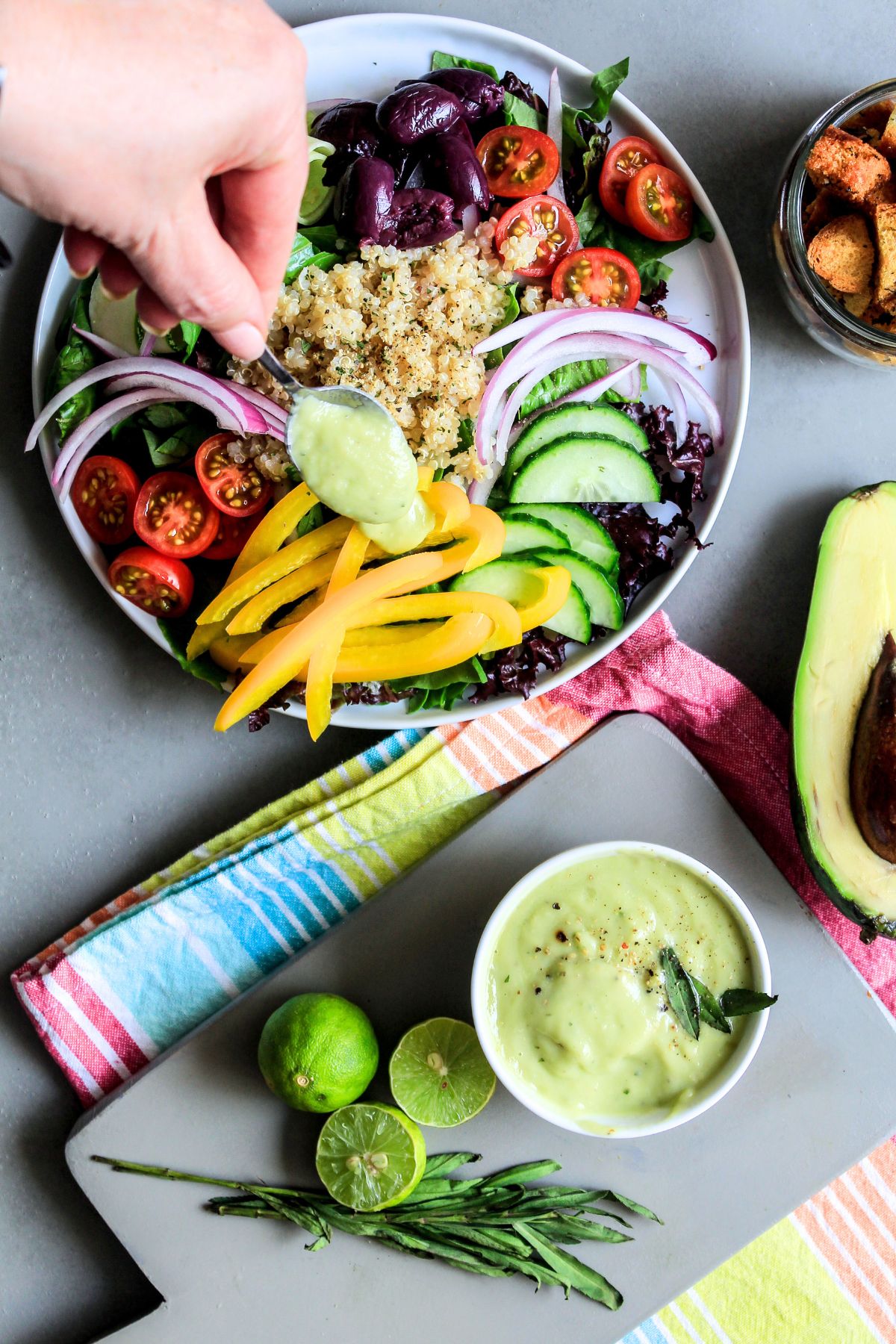 A hand spooning some avocado lime dressing over a salad on the table.