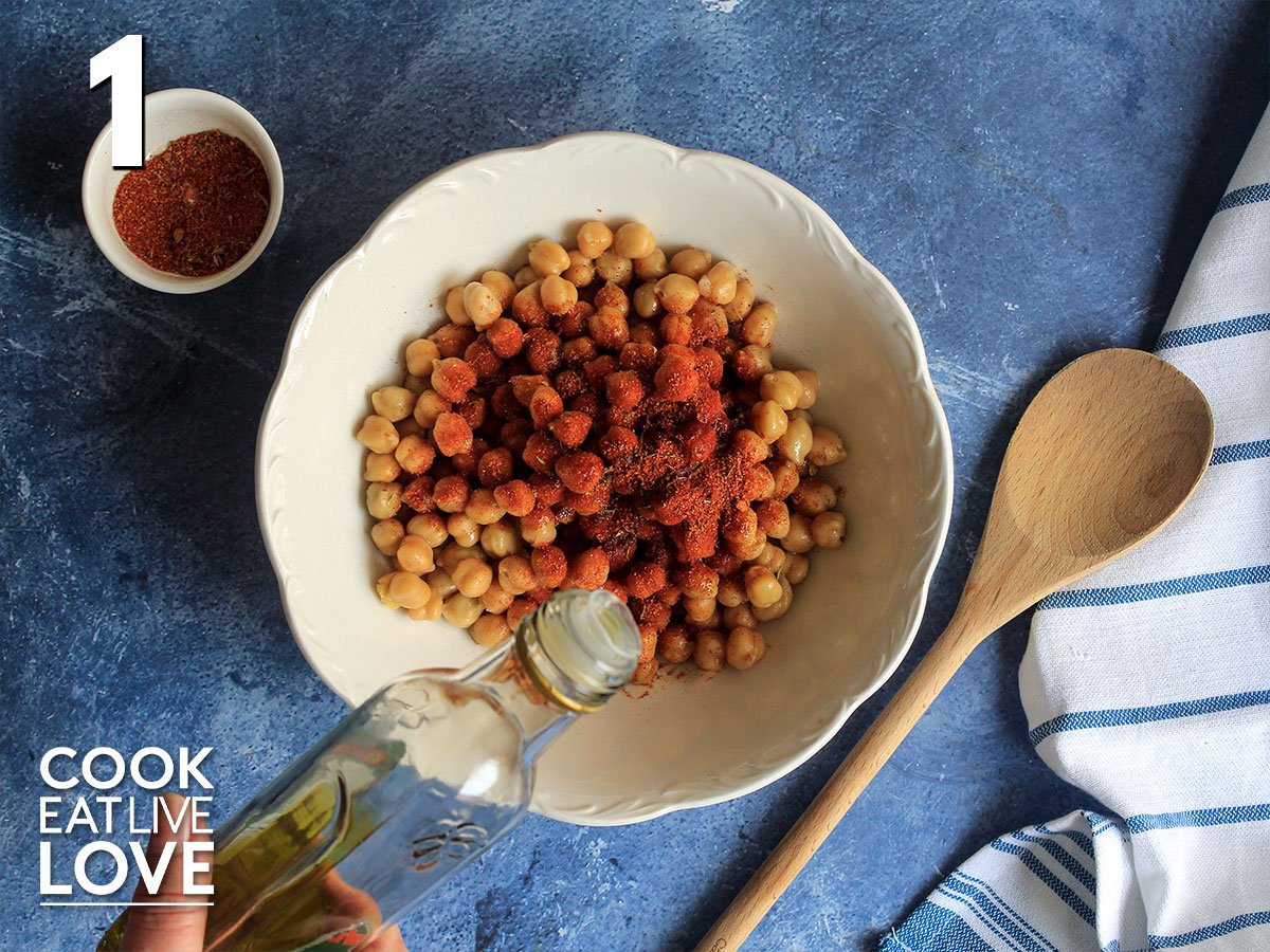 Chickpeas in a bowl with blackening spices and oil drizzling over top