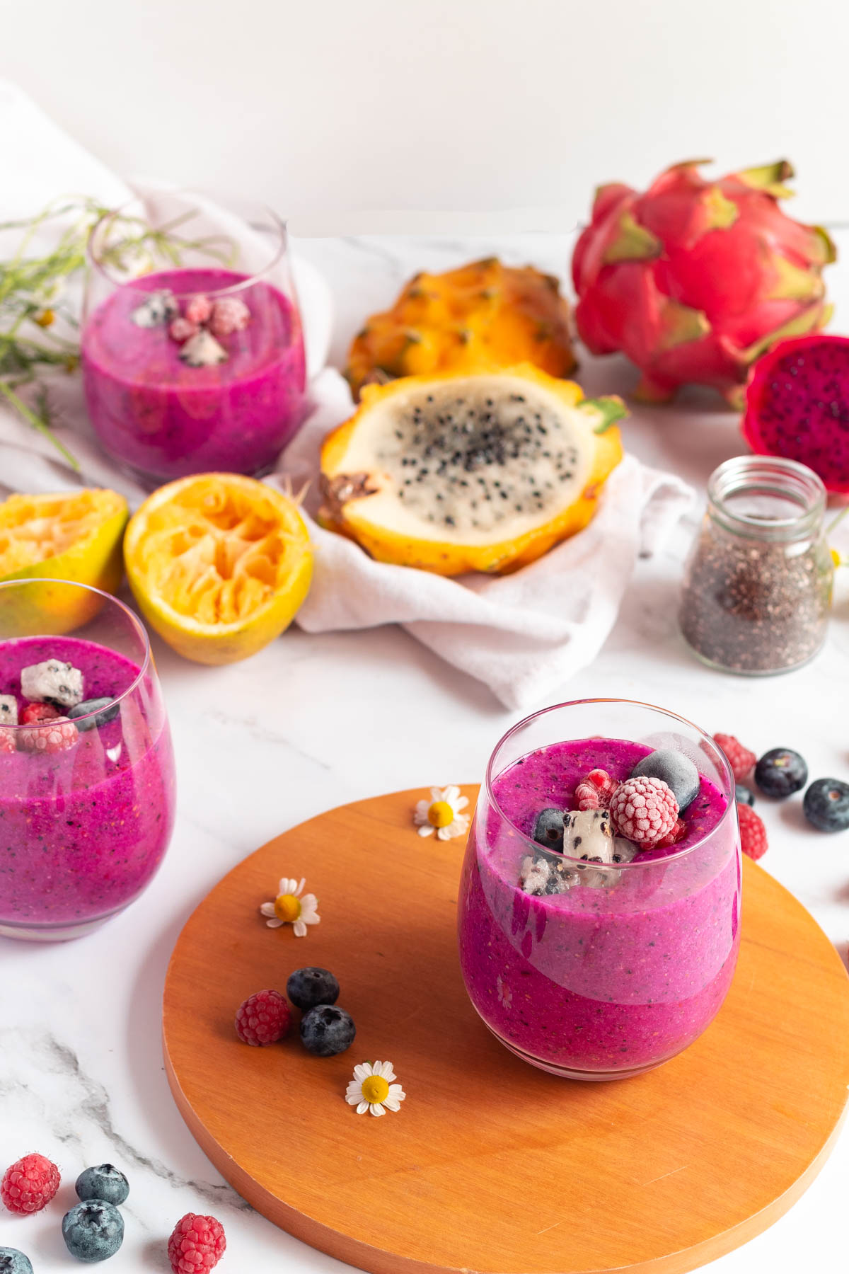 Dragon fruit smoothie in a glass on the table surrounded by cut fruit and berries.