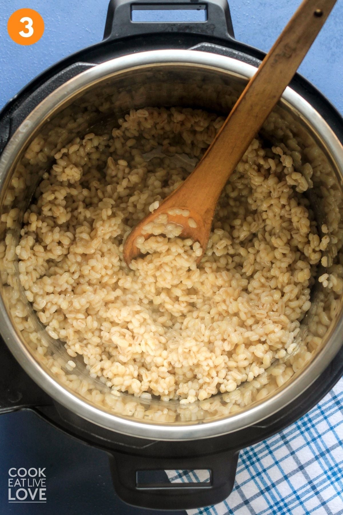 Cooked barley in the Instant Pot with a wooden spoon resting to the side. 