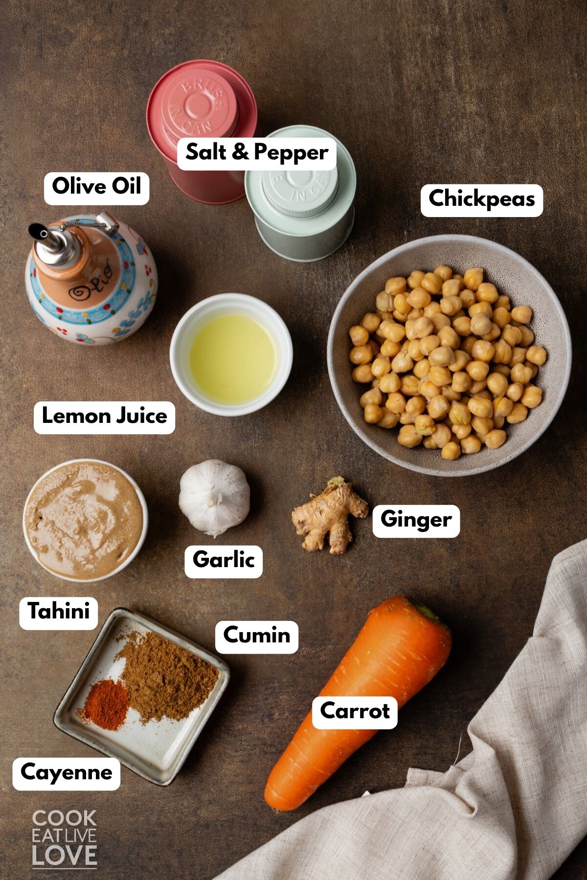Ingredients to make carrot hummus on a brown surface with labels to identify each one.