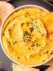 Roasted carrot hummus recipe in a bowl sprinkled with black sesame seeds.