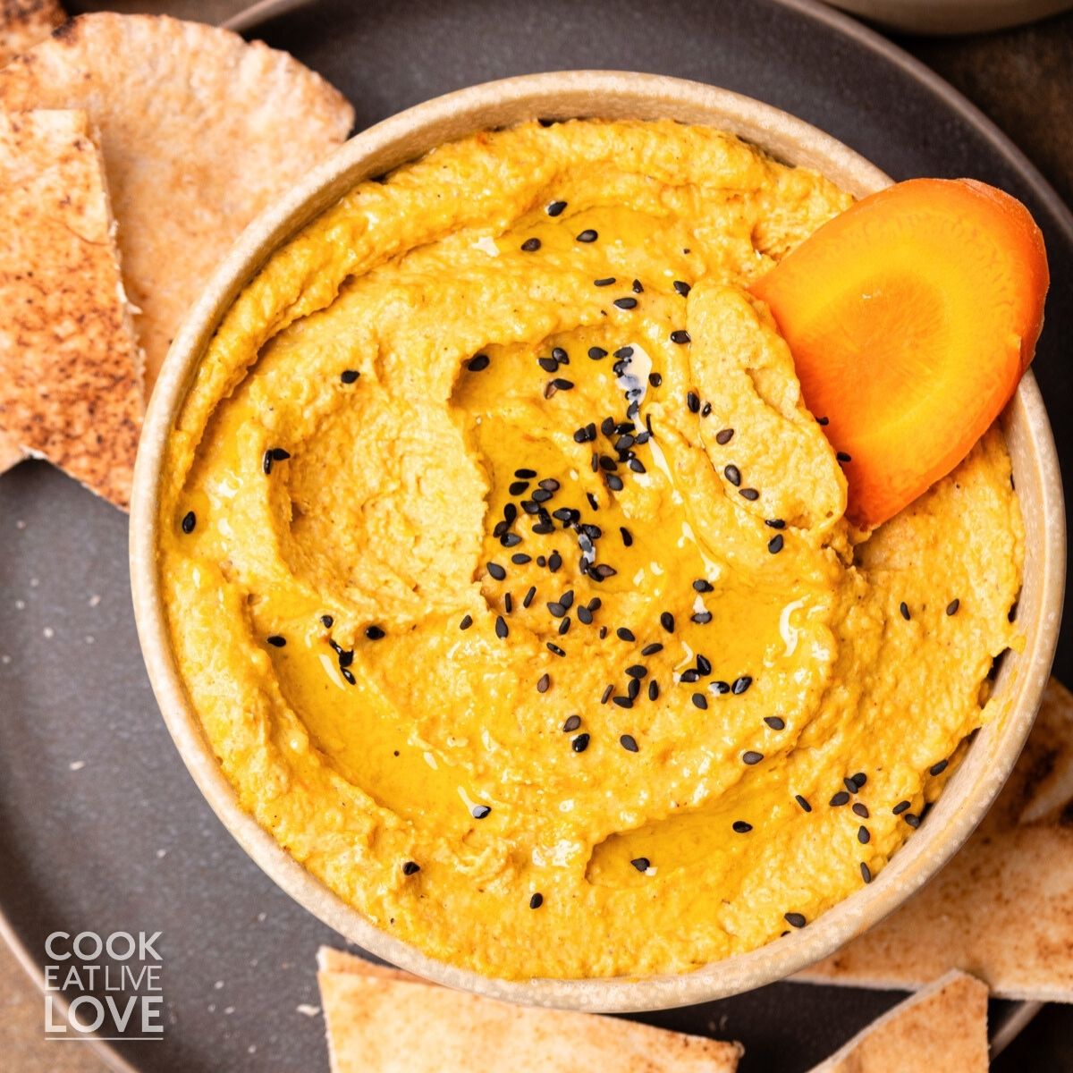 Roasted carrot hummus recipe in a bowl sprinkled with black sesame seeds.