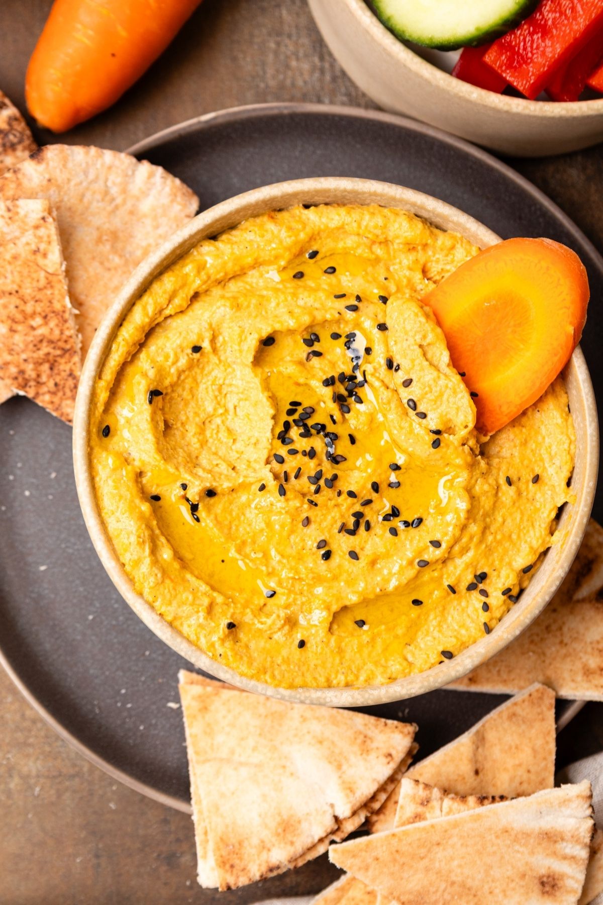A bowl of roasted carrot hummus with pita bread on the side.