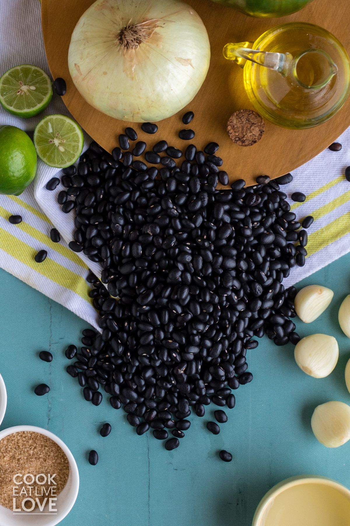 A pile of black beans on a blue backdrop with other ingredients around them.