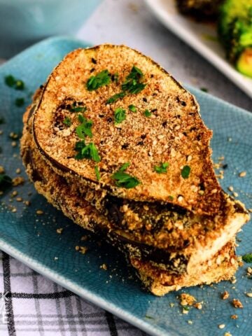 Three slices of crispy breaded eggplant stacked on a blue plate.