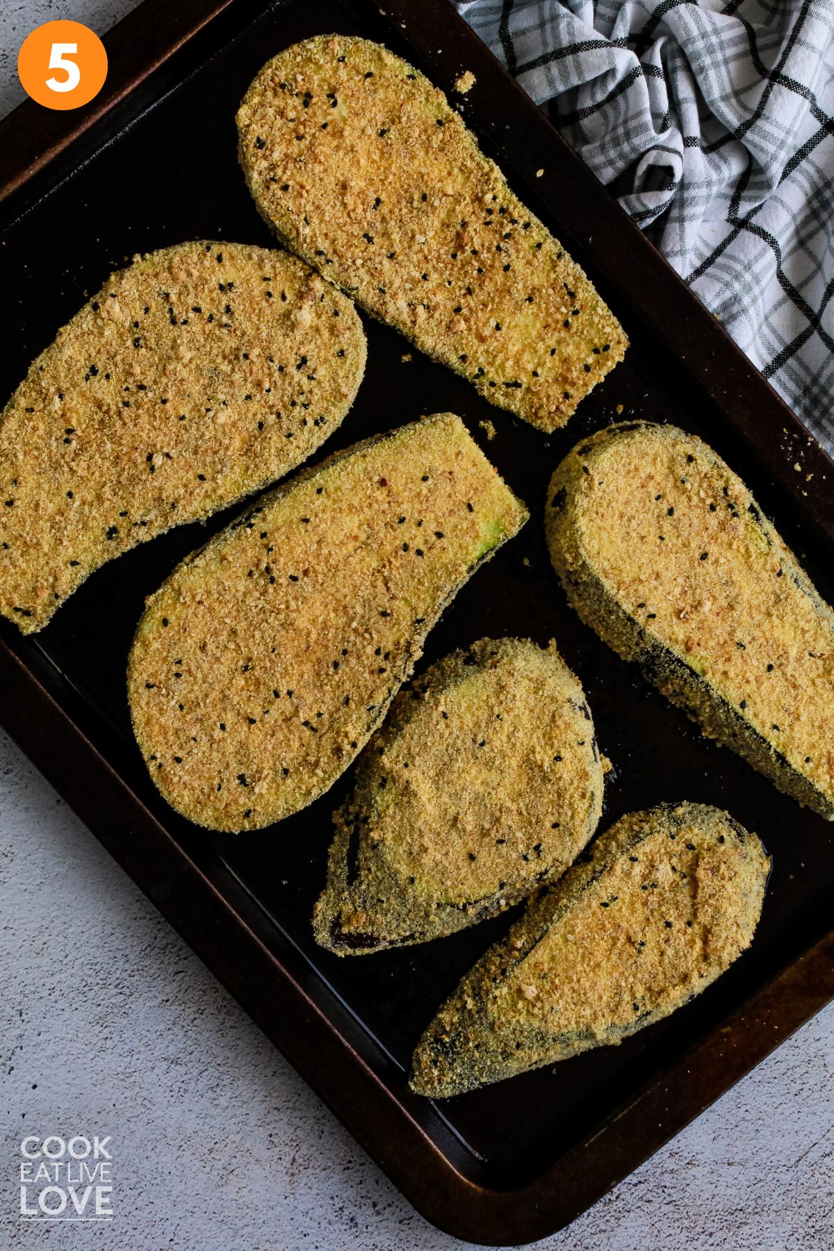 Eggplant placed on a baking pan after coating it in breadcrumbs.