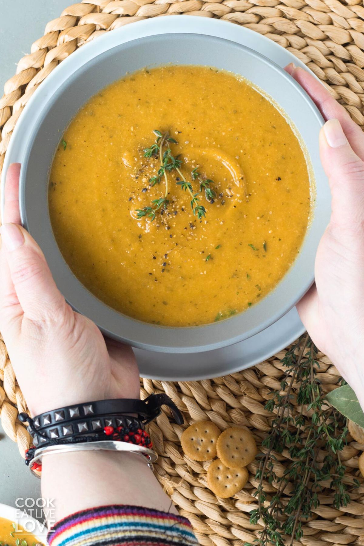 Hands holding a bowl of cauliflower carrot soup on a table. 