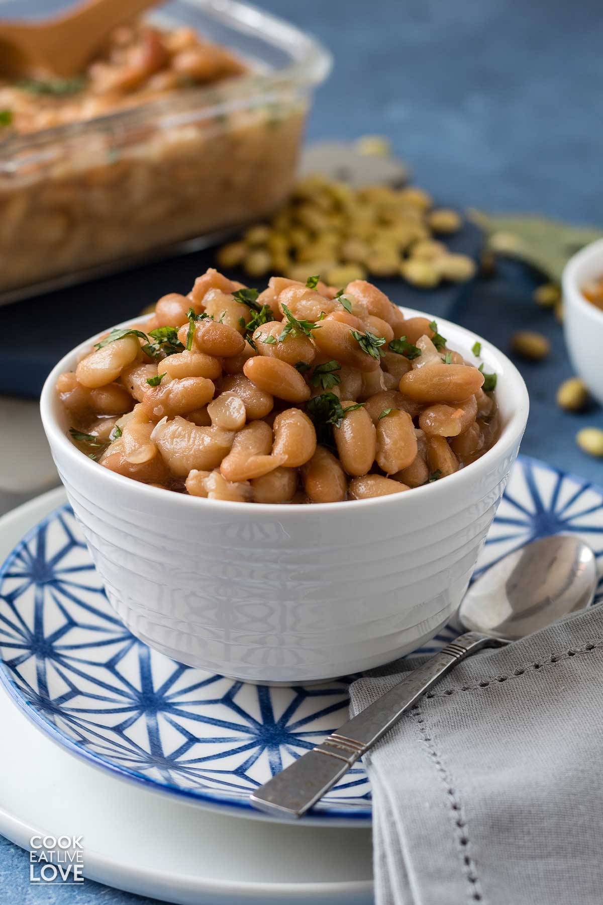 White bowl of cooked mayocoba beans on the table with spoon