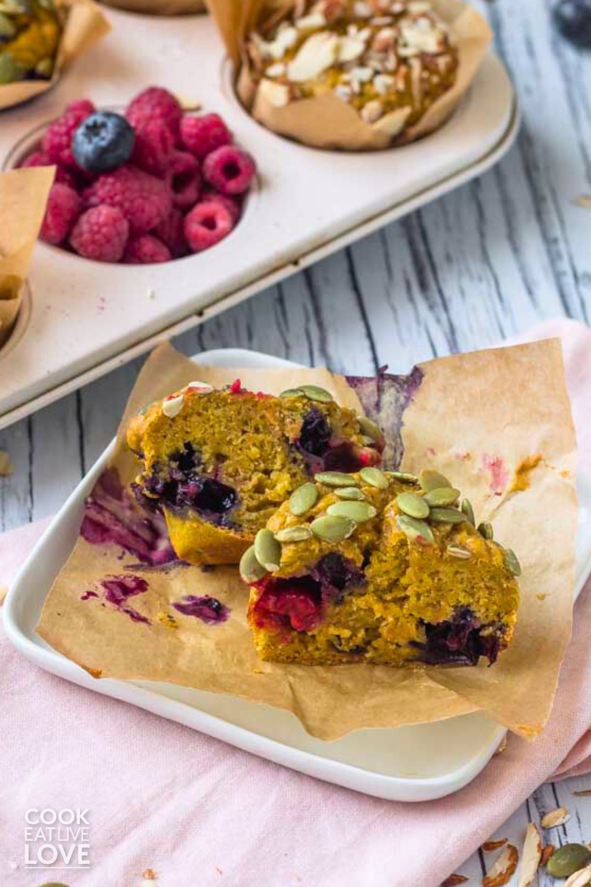 Vegan pumpkin muffin cut in half on a plate to show inside with muffin pan in the background.