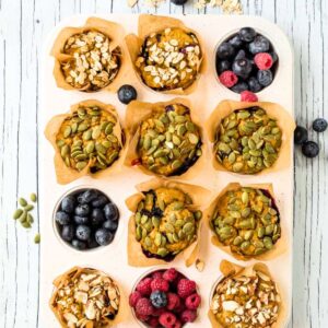 Vegan pumpkin muffins in a muffin pan with berries in a few of the holes.