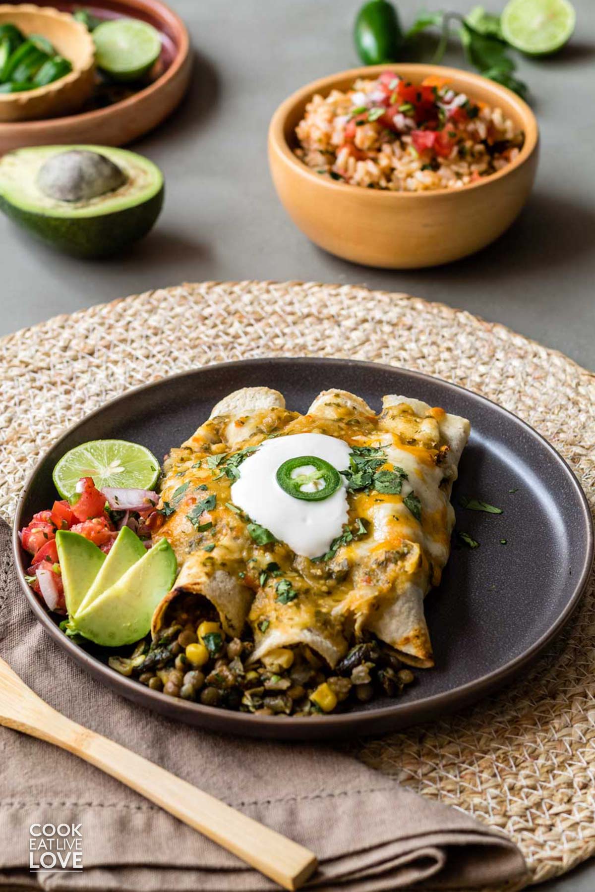 Three vegetarian green enchiladas on a plate with sour cream and a slice of jalapeno