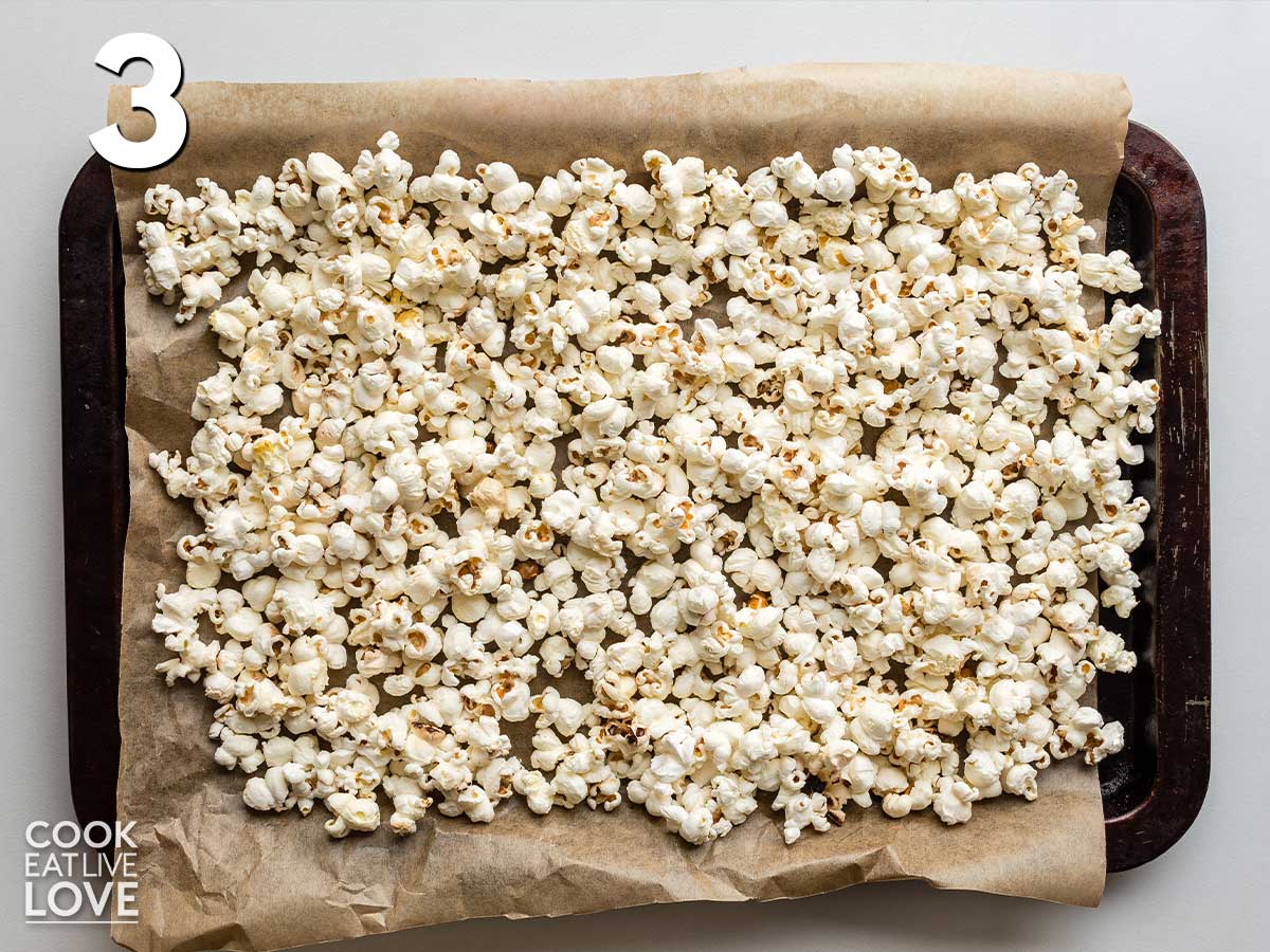 Popped popcorn is spread out on a baking sheet in an even layer.