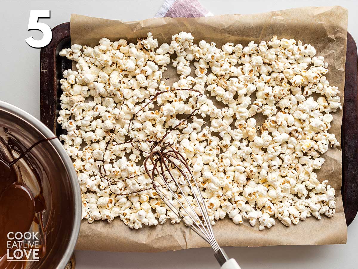 Using a whisk to drizzle the chocolate on top of the popcorn.
