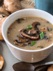 A bowl of mushroom soup without cream with a spoon in front and some crackers on the side.