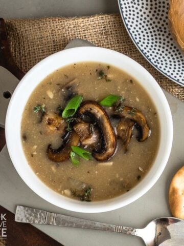 A bowl of mushroom soup without cream on a gray cutting board with a spoon to the side.