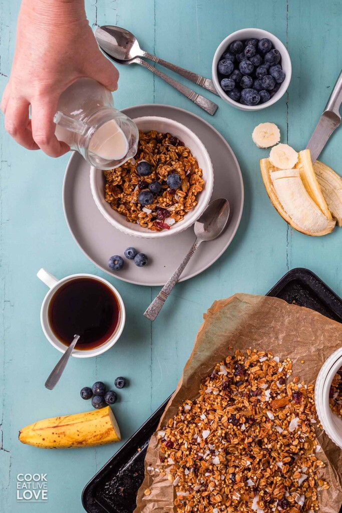 Table with nut free granola in a bowl and a hand pouring milk in.
