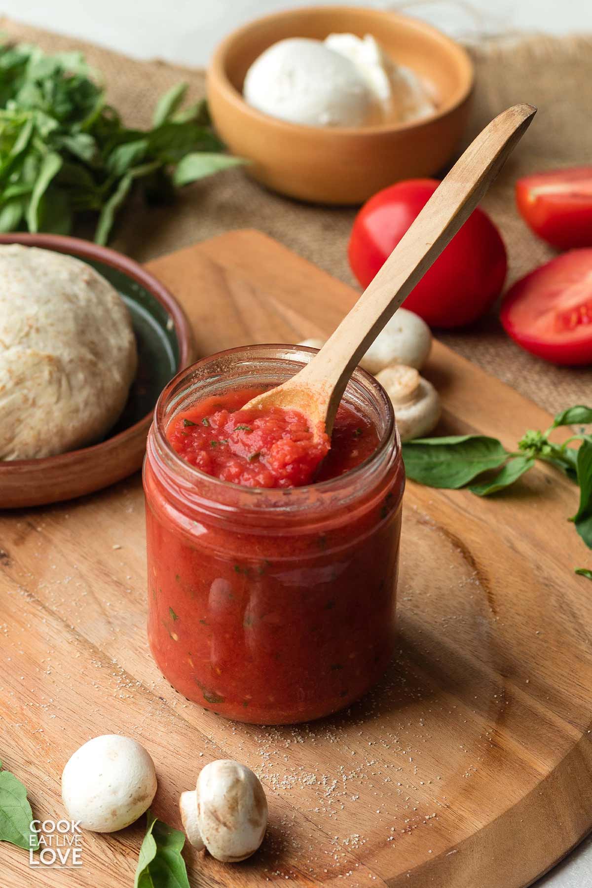 A jar of homemade pizza sauce using fresh tomatoes on the table with a spoon dipping some out.