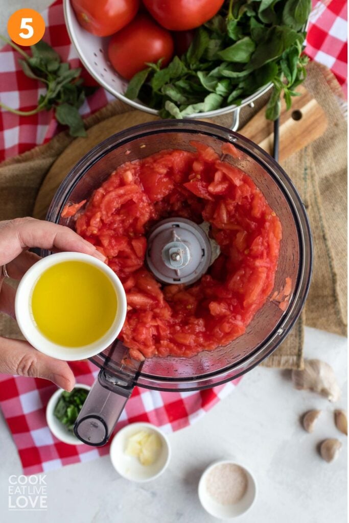 Adding olive oil to the chopped tomatoes in the food processor.