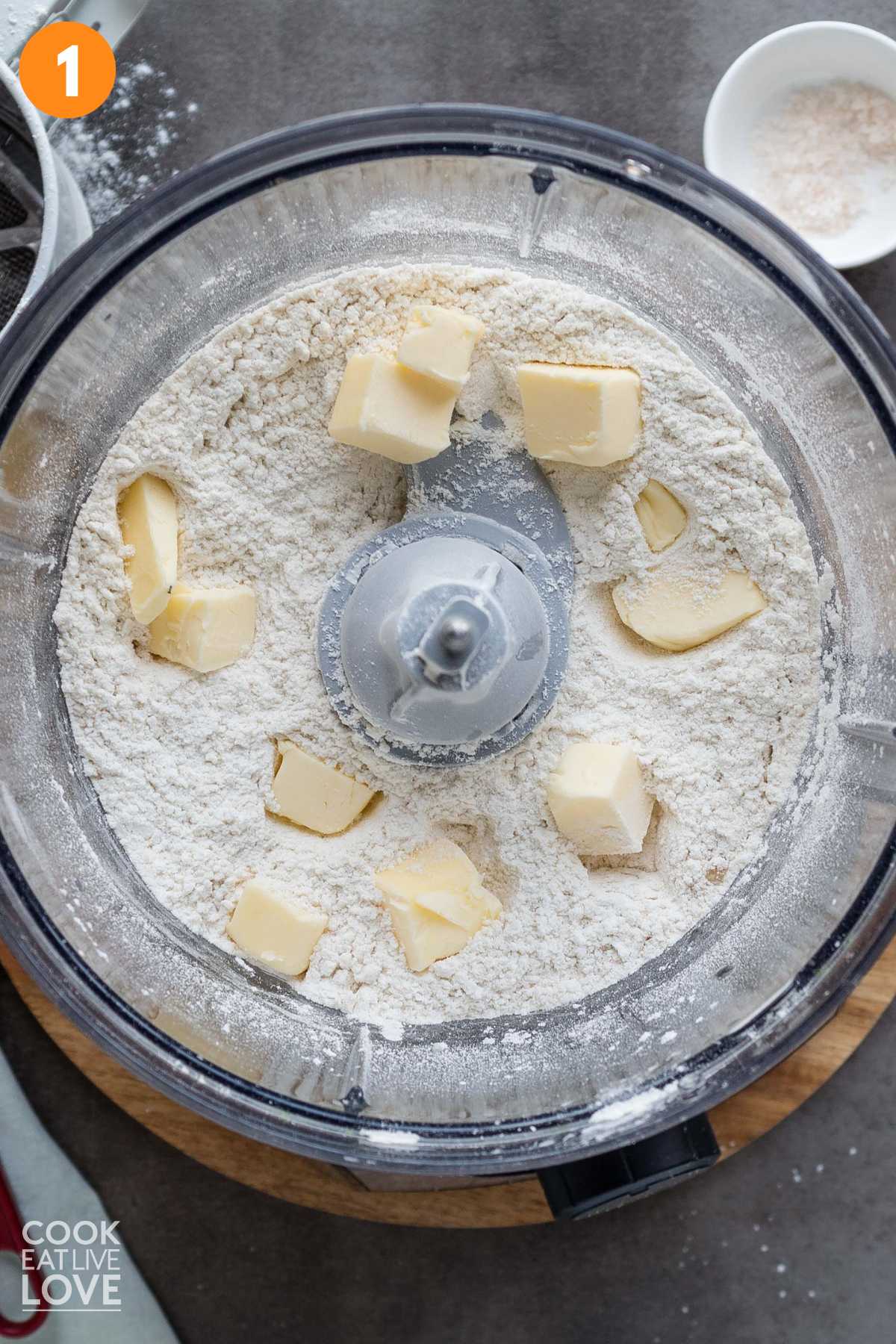 Flour in a food processor bowl with pats of butter on top.