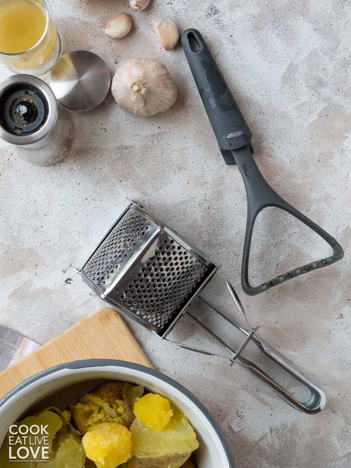 Potato ricer and masher on the table with mashed potato ingredients.