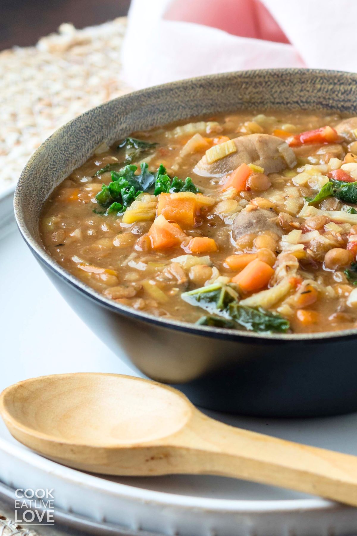 A half bowl of lentil mushroom stew on the table with a small wooden spoon to the side.