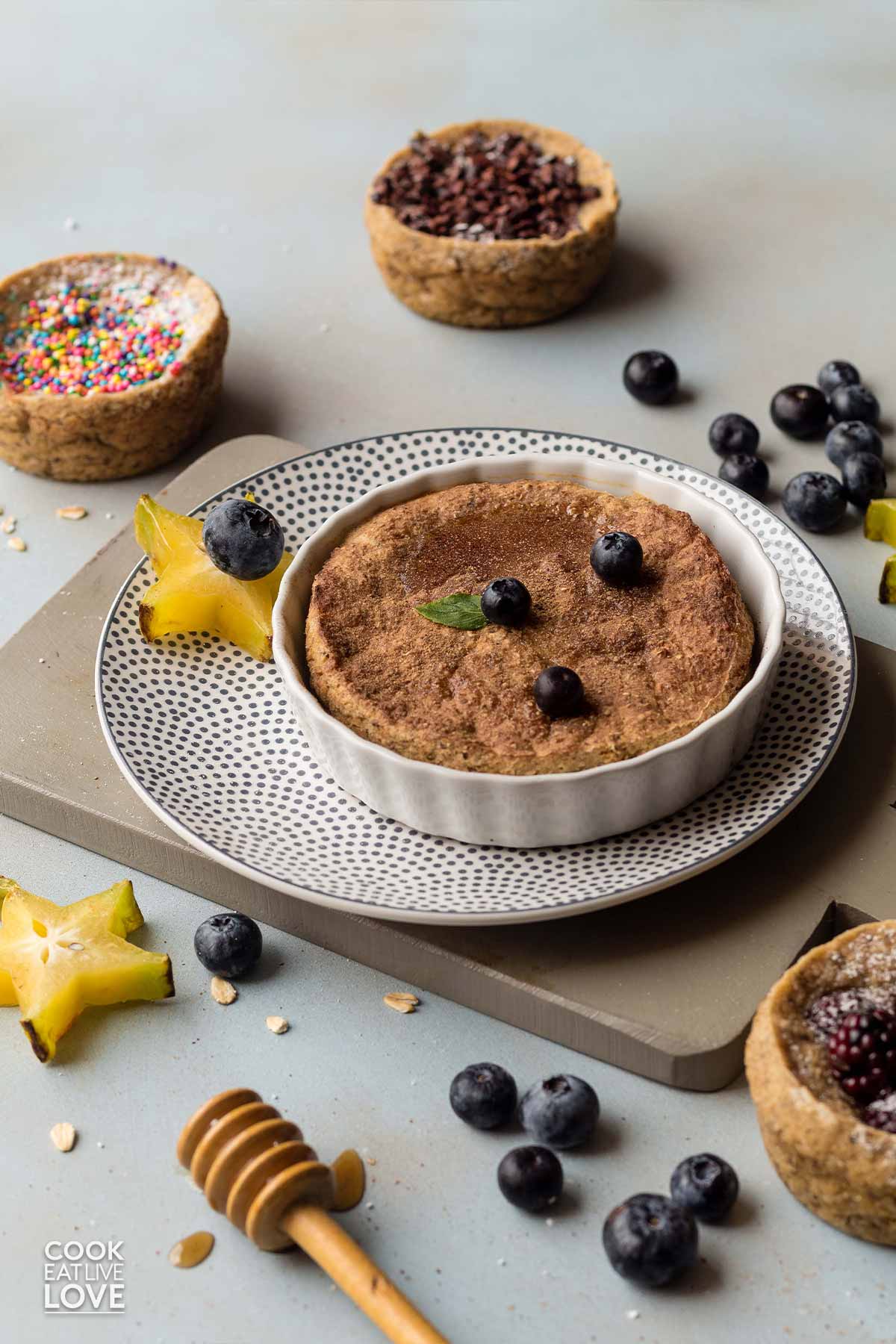 Healthy baked oats for one on a plate with berries and other flavors in background.