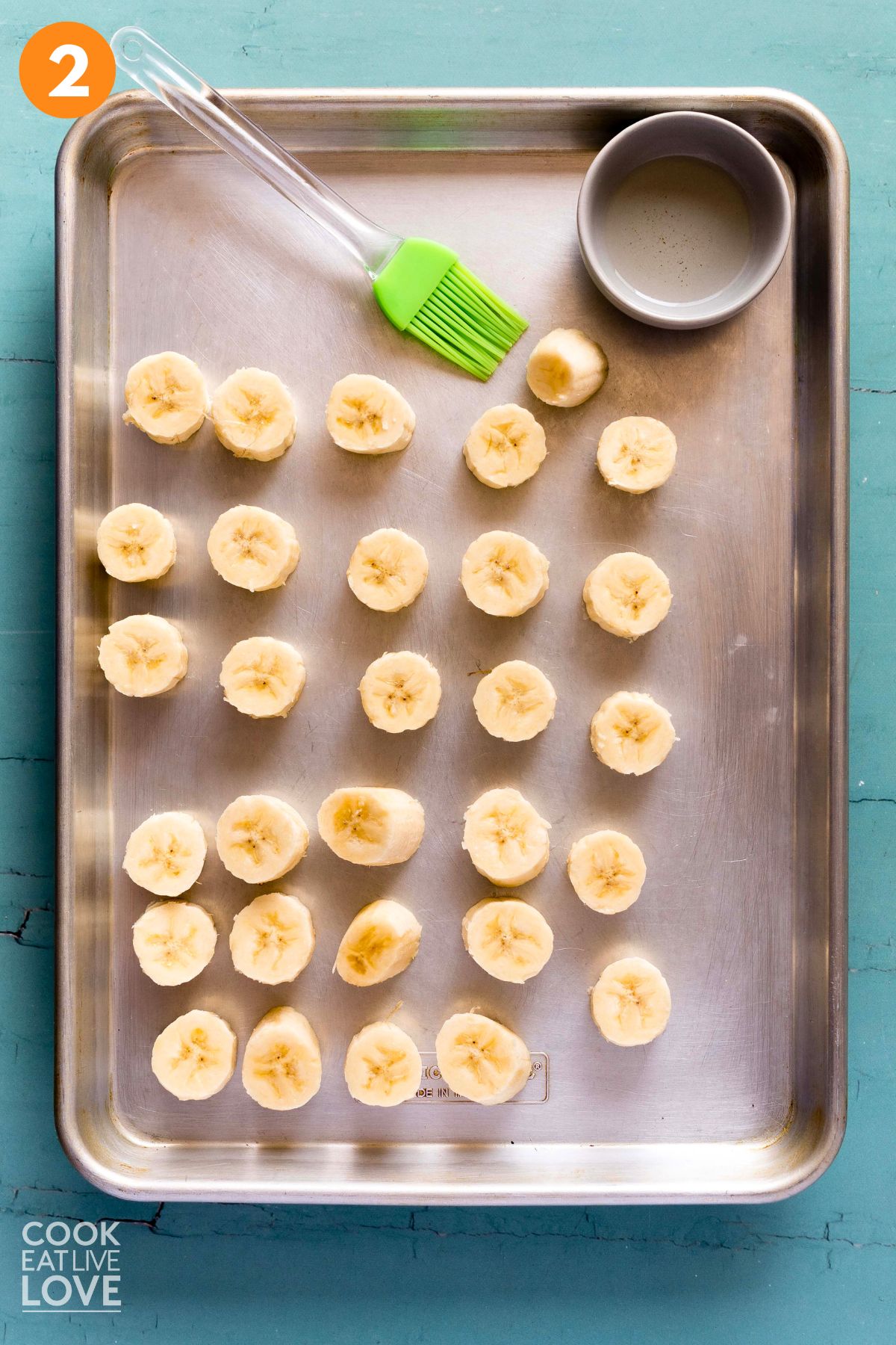 Sliced bananas laid out on a baking tray with a pastry brush to the side.
