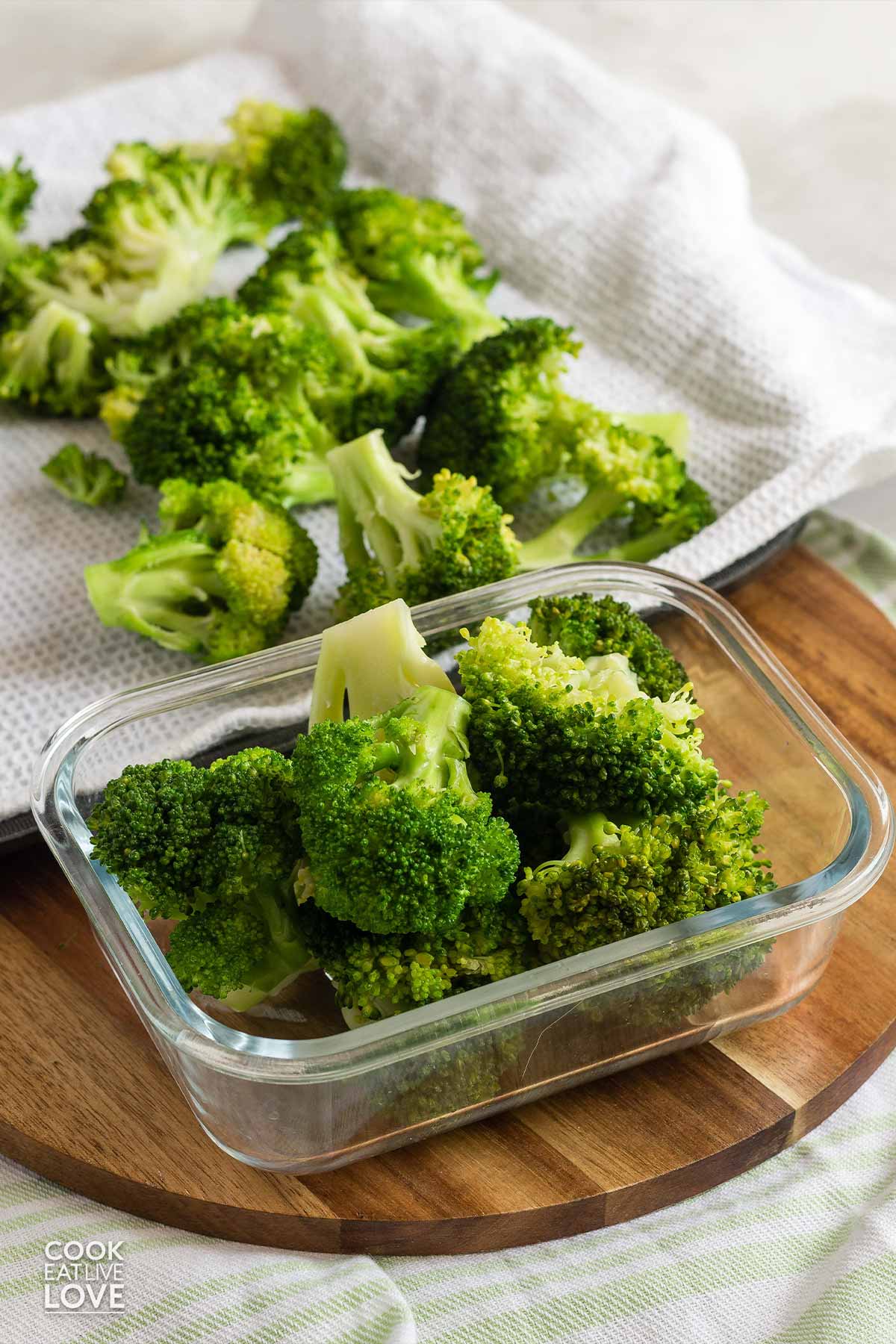 Blanched broccoli in a small container with a tray behind the container.
