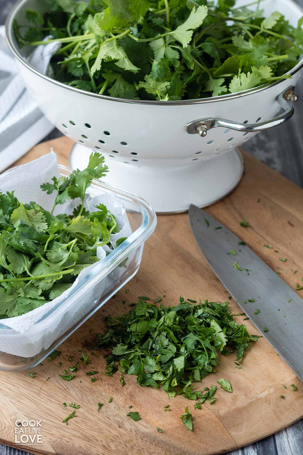 Chopped cilantro leaves next to a container and colander of cilantro on the cutting board.